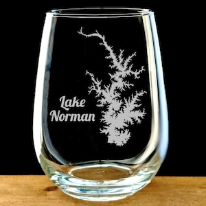 May include: A clear glass stemless wine glass with an etched design of Lake Norman. The text "Lake Norman" is also etched on the glass.