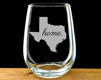 May include: A clear glass stemless wine glass with an etched outline of the state of Texas and the word "home."