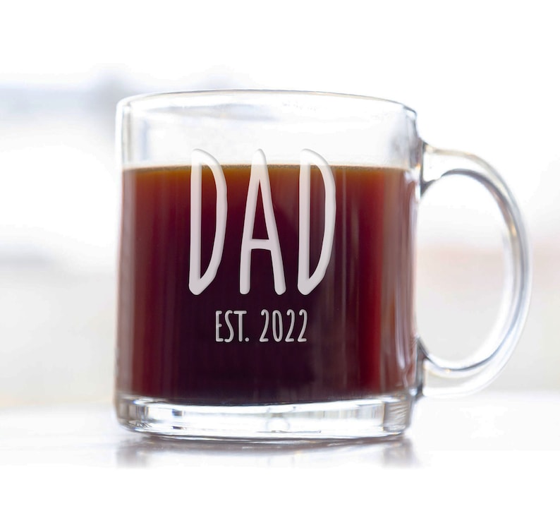Puede incluir: Una taza de caf&eacute; de vidrio transparente con caf&eacute; negro en su interior. La taza tiene las palabras "DAD EST. 2022" grabadas en el lateral.