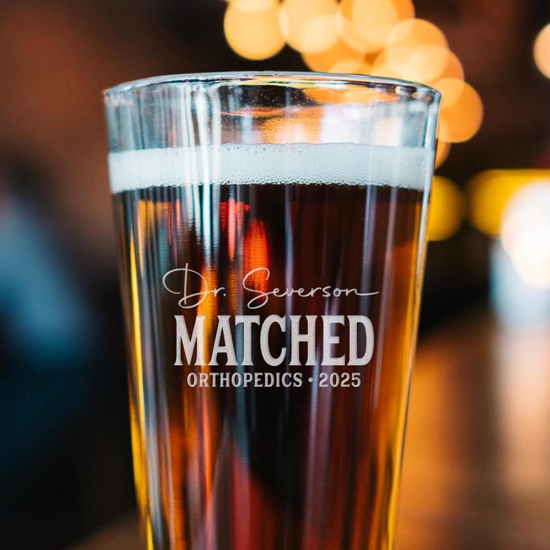 May include: A clear glass beer stein with the text "Dr. Severson MATCHED ORTHOPEDICS - 2025" etched on the side. The stein is filled with a dark brown beer.