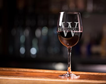 May include: A clear glass wine glass with a stem and a wide bowl. The glass is filled with red wine and has the letter "W" and the word "WILLIAMS" etched on the side.