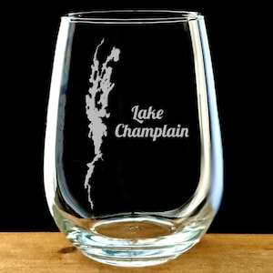 May include: A clear glass stemless wine glass with an etched design of Lake Champlain and the text "Lake Champlain".