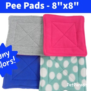 May include: Four 8-inch by 8-inch square pee pads in different colors and patterns. The pads are made of soft fleece fabric. The colors are gray, pink, blue, and teal with white polka dots. The text "Many Colors!" is in a blue starburst shape. The text "Pet Paradis" is in the bottom right corner.