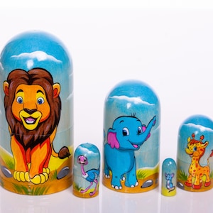 May include: A set of five colorful wooden nesting dolls, or matryoshka dolls, with a blue background and animal illustrations. The largest doll features a lion, the next largest an elephant, the next a giraffe, and the smallest two dolls feature an ostrich and a mouse.