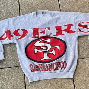 May include: Gray sweatshirt with the words "49ers" and "San Francisco" printed in red. The sweatshirt has a large red logo with the letters "SF" in white.