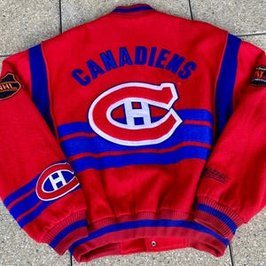 May include: A red and blue vintage Canadiens letterman jacket. The jacket features the team name and logo on the back, with blue stripes and patches on the sleeves. The jacket has a button-up front and ribbed cuffs.