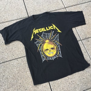 May include: Black t-shirt with a yellow spider and skull graphic. The text "Metallica" is printed in yellow above the spider.