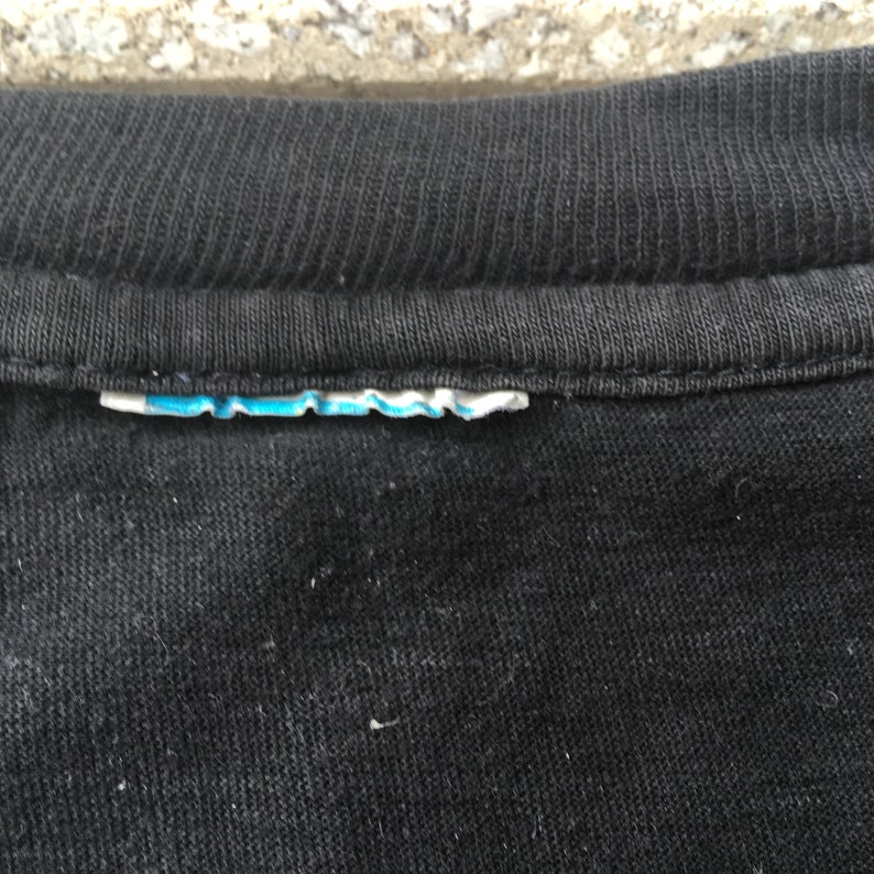 May include: Close-up of a black t-shirt with a blue and white tag sewn into the neckline.