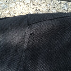May include: Close-up of a black t-shirt with a small hole near the shoulder seam.