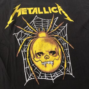 May include: Black t-shirt with a yellow spider skull graphic and the word "METALLICA" in yellow lettering.