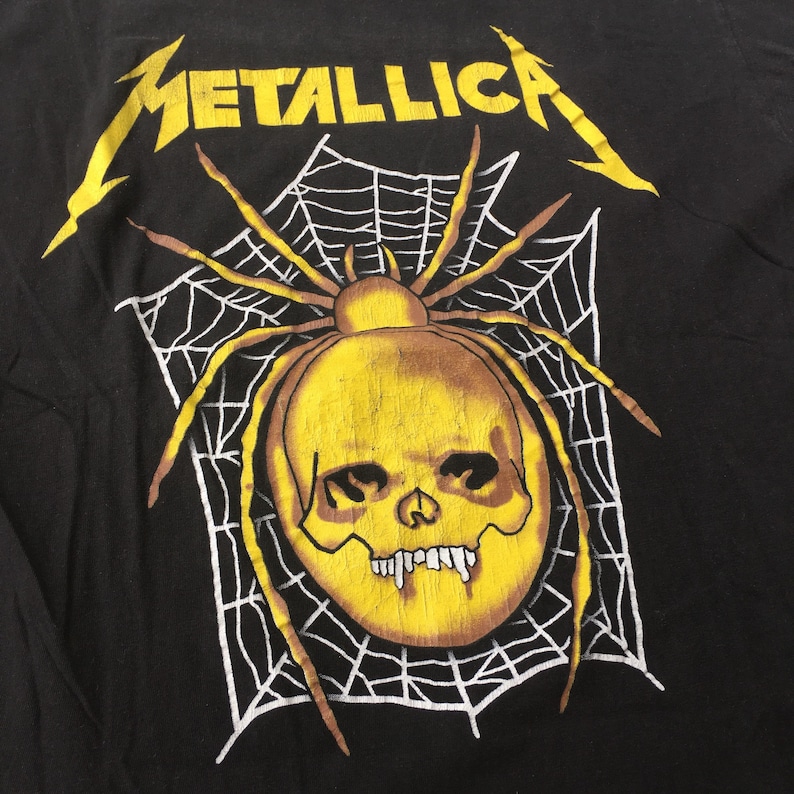 May include: Black t-shirt with a yellow spider skull graphic and the word "METALLICA" in yellow lettering.