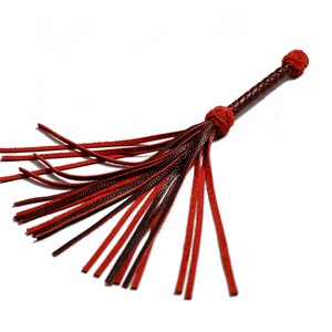 May include: A red and brown leather whip with a braided handle and multiple strands of leather hanging from the end.