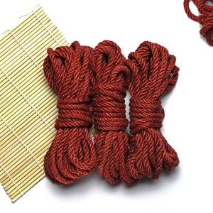May include: Three spools of thick, red rope, coiled and ready for use. The rope is made of a natural fiber and has a rustic look.