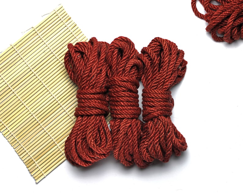 May include: Three spools of thick, red rope, coiled and ready for use. The rope is made of a natural fiber and has a rustic look.