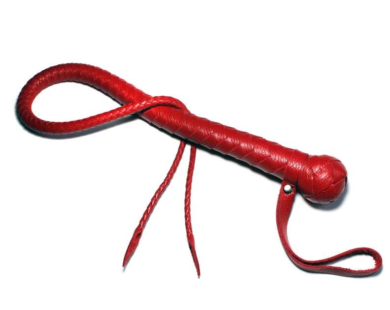 May include: A red leather whip with a braided handle and a knotted end. The whip has a strap attached to the handle.