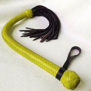 May include: A yellow leather whip with a braided handle and a brown leather tassel. The whip has a braided handle and a knotted end.