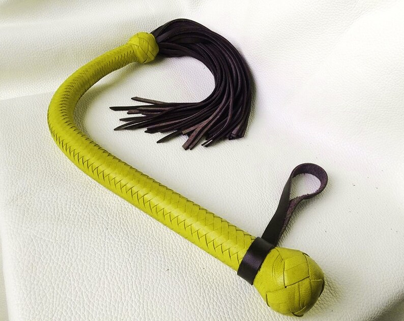 May include: A yellow leather whip with a braided handle and a brown leather tassel. The whip has a braided handle and a knotted end.
