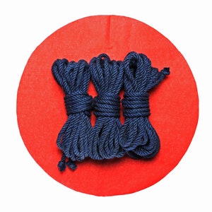 May include: Three spools of dark blue rope on a red background.
