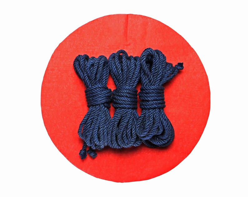May include: Three spools of dark blue rope on a red background.