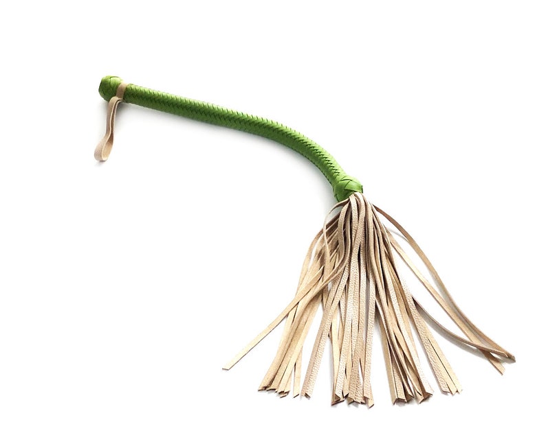 May include: A green leather whip with a tan leather fringe. The whip is made of braided leather and has a loop at the end.