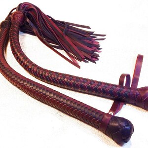 May include: A pair of braided leather whips with burgundy and black leather. The whips have a tassel at the end and a loop at the handle.