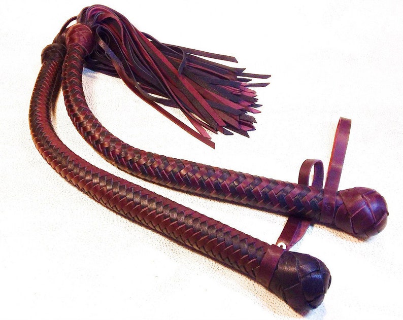 May include: A pair of braided leather whips with burgundy and black leather. The whips have a tassel at the end and a loop at the handle.