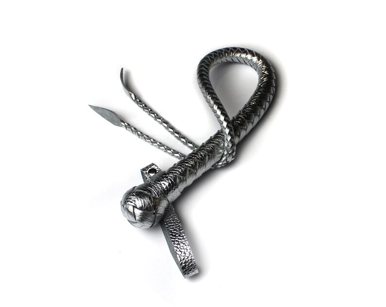 May include: A silver braided leather whip with a knotted handle and a long, thin tail.