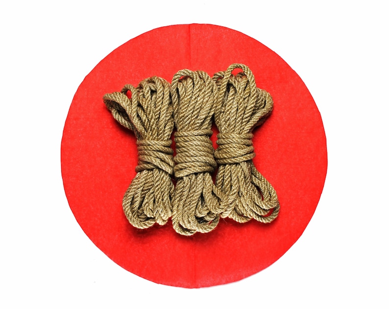 May include: Three golden ropes are arranged on a red circular surface. The ropes are made of a thick, braided material and are tied together in the center.
