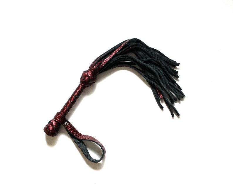 May include: A red leather whip with a black tassel. The whip has a braided handle and a loop for holding.