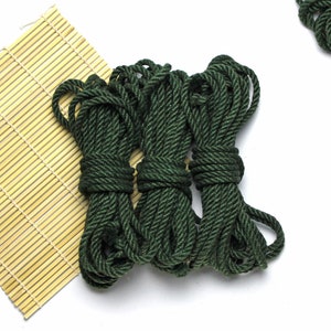 May include: Three spools of dark green rope are stacked on top of each other. The rope is thick and has a textured surface.