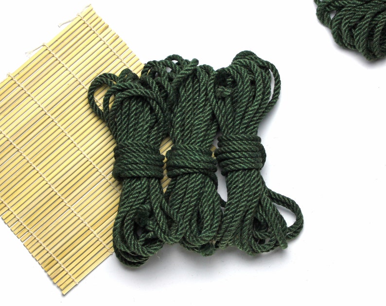 May include: Three spools of dark green rope are stacked on top of each other. The rope is thick and has a textured surface.