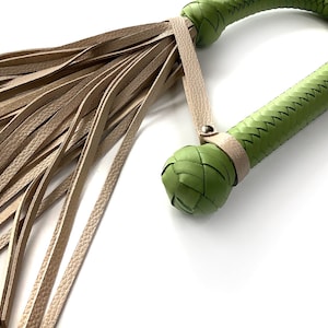 May include: A green leather whip with a braided handle and a long, fringed tassel. The whip is made of high-quality leather and is designed for use in a variety of settings.