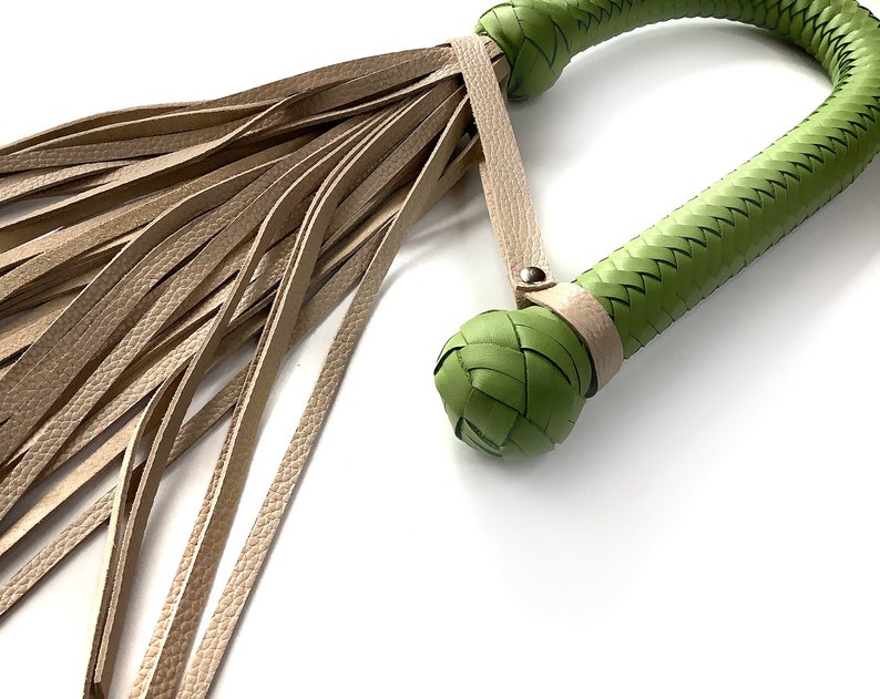 May include: A green leather whip with a braided handle and a long, fringed tassel. The whip is made of high-quality leather and is designed for use in a variety of settings.