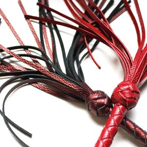 May include: Two leather whips with braided handles and tassels. One whip is black and the other is red.