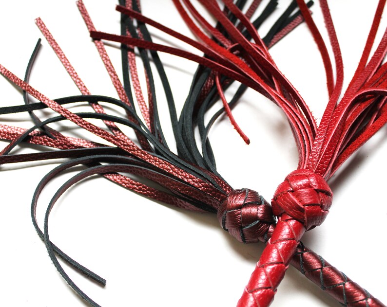 May include: Two leather whips with braided handles and tassels. One whip is black and the other is red.