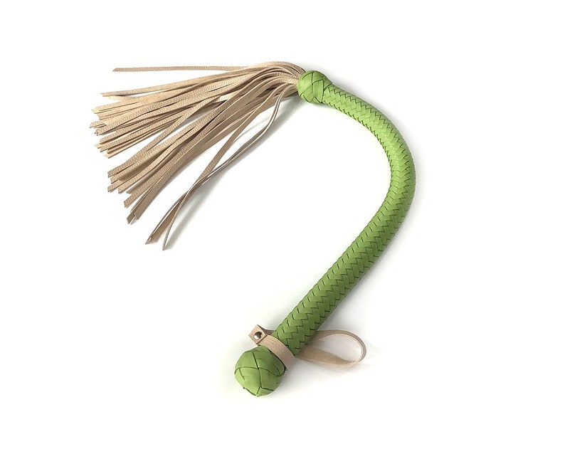 May include: A green leather whip with a braided handle and a tan leather tassel.