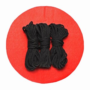May include: Three spools of black rope on a red circular background.