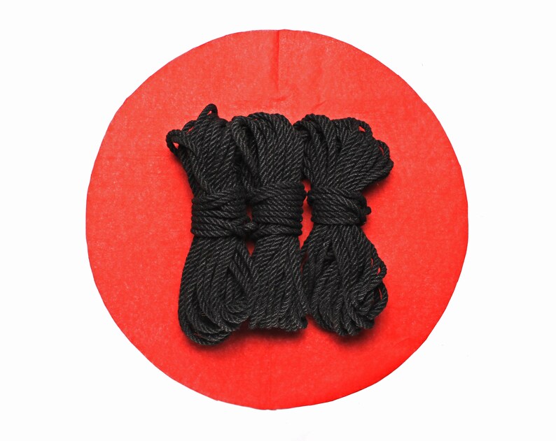May include: Three spools of black rope on a red circular background.