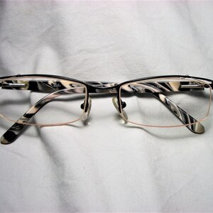 May include: Black and white patterned eyeglasses with a thin metal frame. The frame has a subtle pink tint.