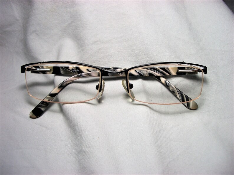 May include: Black and white patterned eyeglasses with a thin metal frame. The frame has a subtle pink tint.