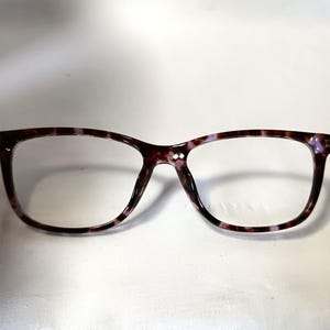Peut inclure: Lunettes rectangulaires avec une monture &agrave; motif &eacute;caille de tortue marron fonc&eacute; et violet. Les lunettes ont des verres transparents et un style classique. La monture est faite d'un mat&eacute;riau durable.