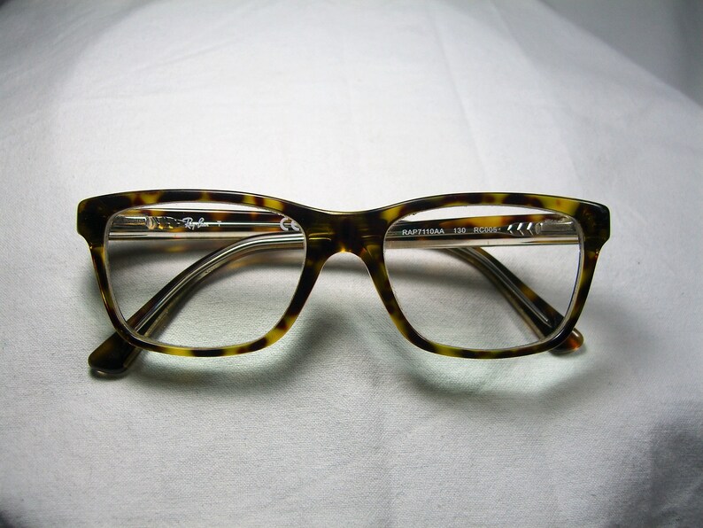 May include: Tortoise shell eyeglasses with a clear lens and the text "RAP7110AA 135 RC004" printed on the side.