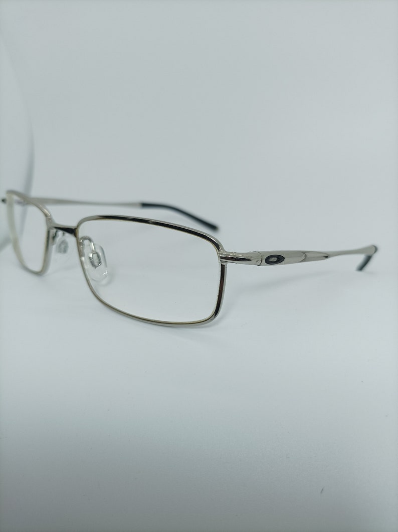 Puede incluir: Gafas rectangulares plateadas con detalles negros en las patillas.