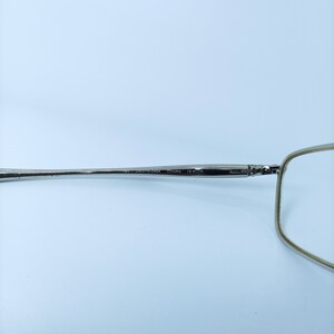 Puede incluir: Gafas de metal plateadas con montura rectangular y una fina varilla de metal. La varilla est&aacute; marcada con "US 33110-143" y "Chrome CE".