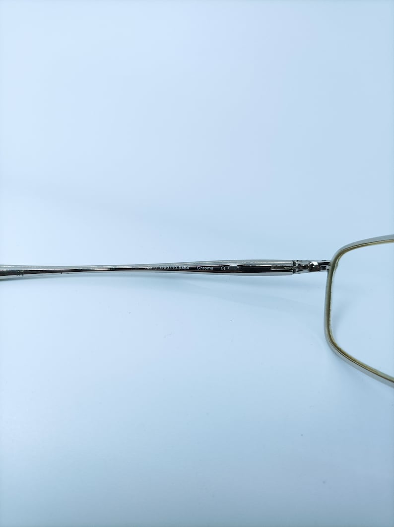 Puede incluir: Gafas de metal plateadas con montura rectangular y una fina varilla de metal. La varilla est&aacute; marcada con "US 33110-143" y "Chrome CE".