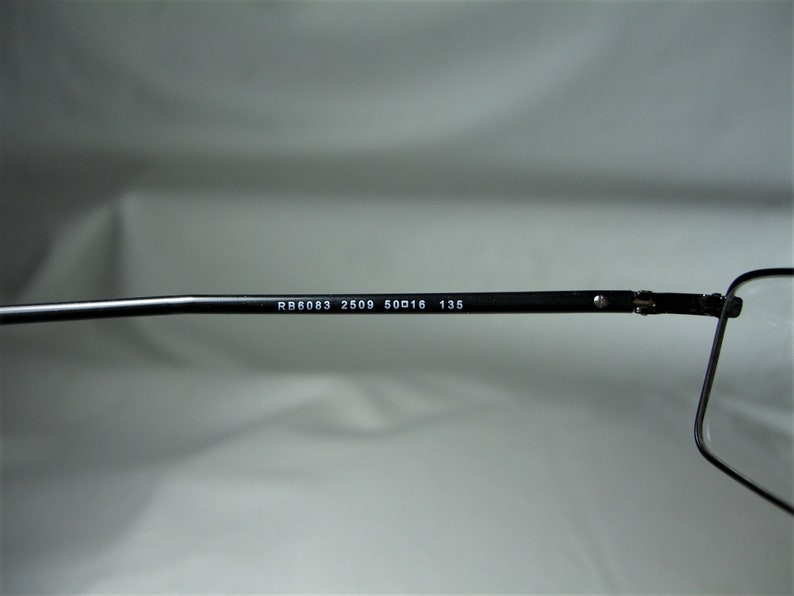 Puede incluir: Primer plano del brazo de unas gafas negras con el texto "RB6083 2509 50□16 135" impreso en el brazo.
