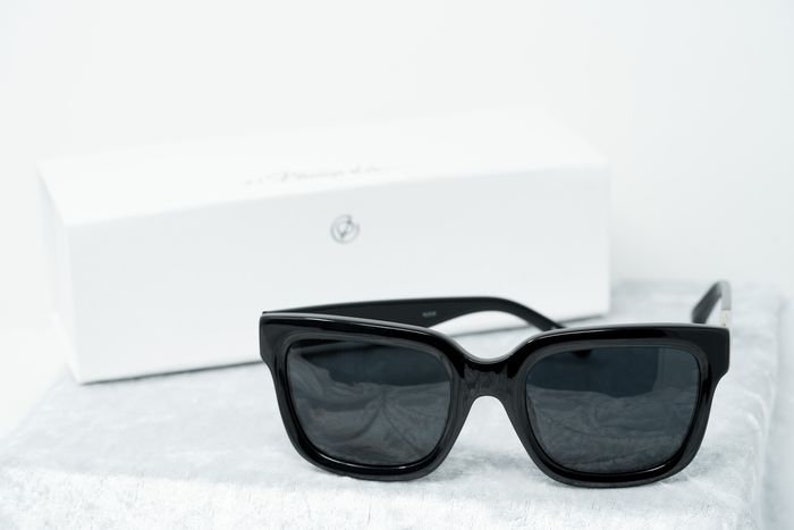 Puede incluir: Gafas de sol cuadradas negras con lentes oscuros. Las gafas de sol est&aacute;n sobre una superficie blanca.