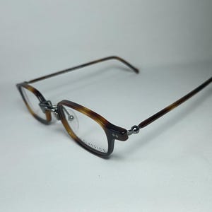 May include: Eyeglasses with a tortoiseshell pattern on the frames and temples. The rectangular lenses are clear, and the frames are connected with silver-colored hinges. The glasses are set against a white background.