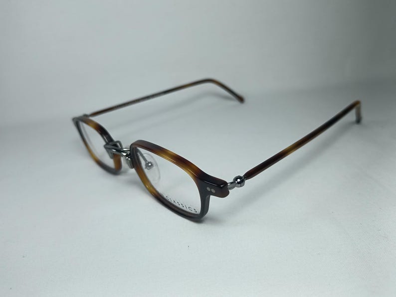 May include: Eyeglasses with a tortoiseshell pattern on the frames and temples. The rectangular lenses are clear, and the frames are connected with silver-colored hinges. The glasses are set against a white background.