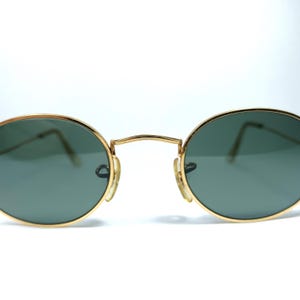 Puede incluir: Gafas de sol redondas con montura dorada y lentes verdes. Las gafas tienen una fina montura de metal.